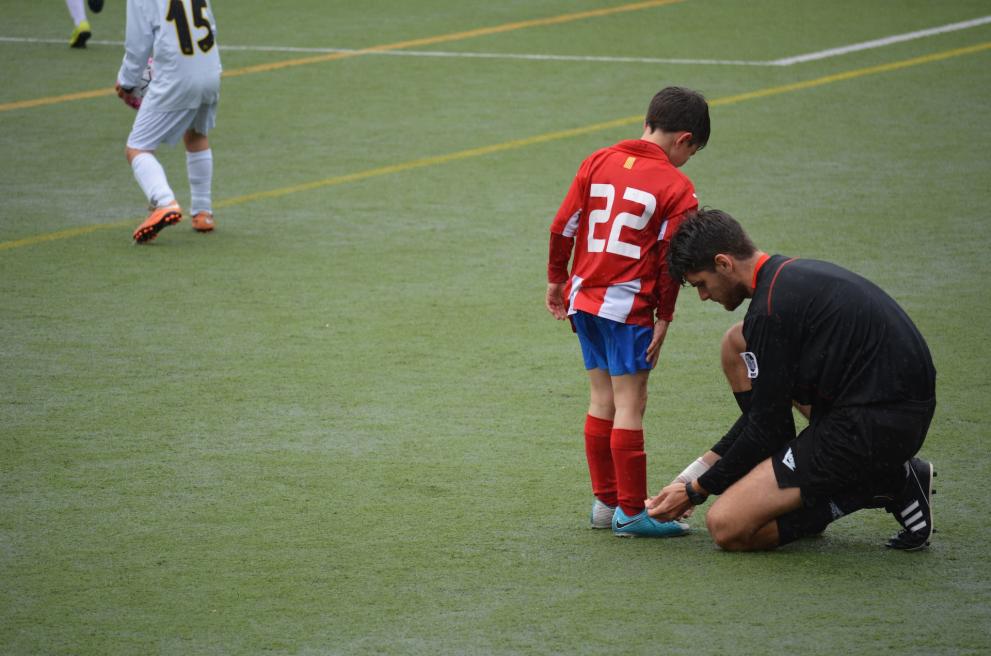 De coach strikt de schoenen van een jonge voetballer